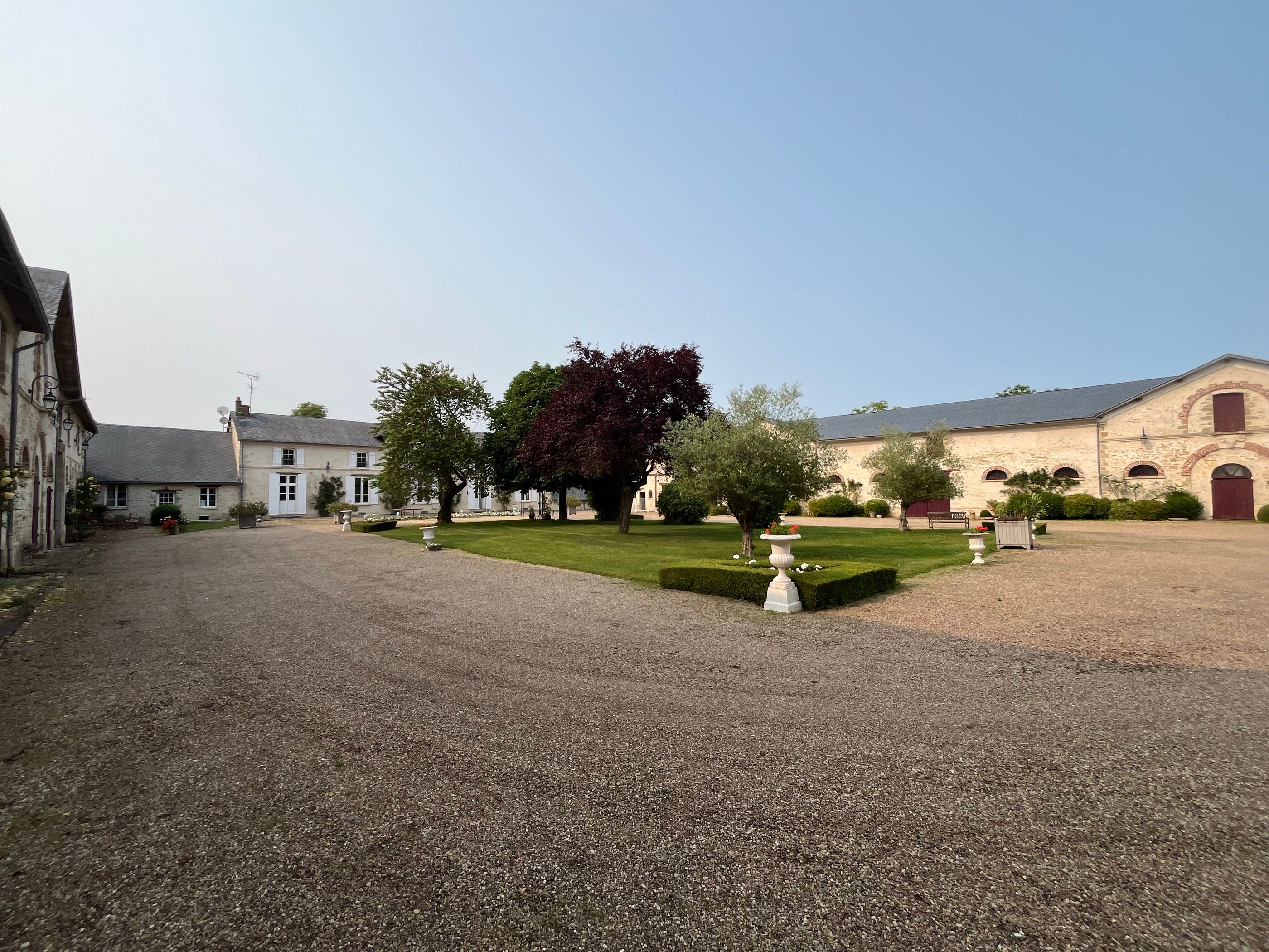 La cour intérieure du Domaine de Solvins vue en grand angle, façades de pierre blonde et charpentes